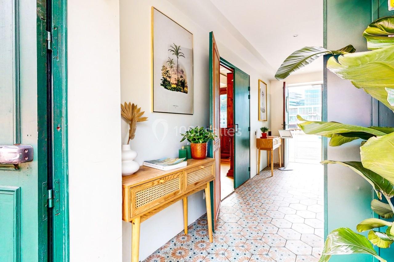 Entrée lumineuse avec sol en carreaux de ciment, mobilier en bois, plantes et portes ouvertes sur une terrasse.