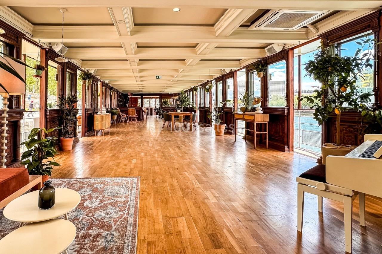 Salle lumineuse avec parquet, grandes fenêtres donnant sur l'extérieur, plantes et mobilier élégant.