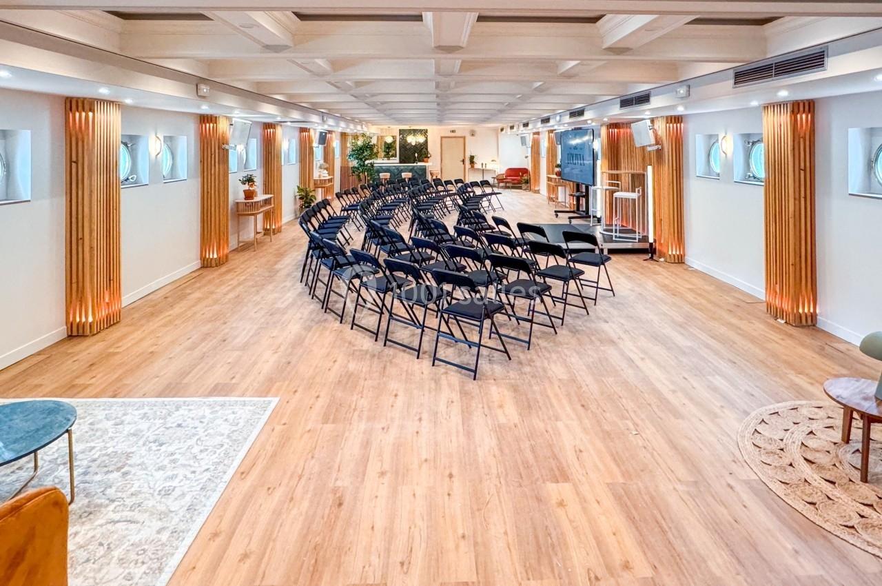 Salle lumineuse avec parquet, rangées de chaises noires disposées pour une présentation, décor moderne et épuré.