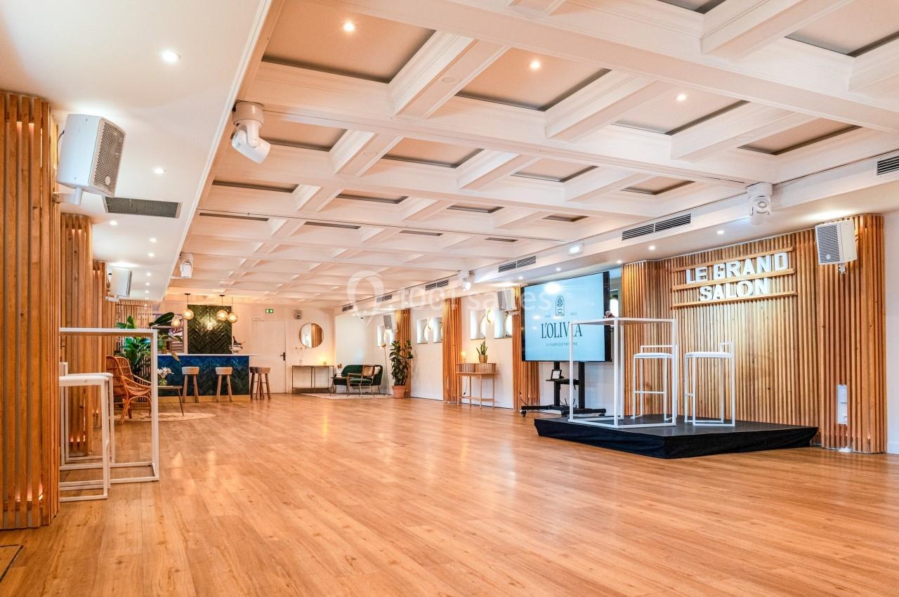 Salle lumineuse avec parquet en bois, murs ornés de panneaux en bois, estrade et écrans pour présentations.