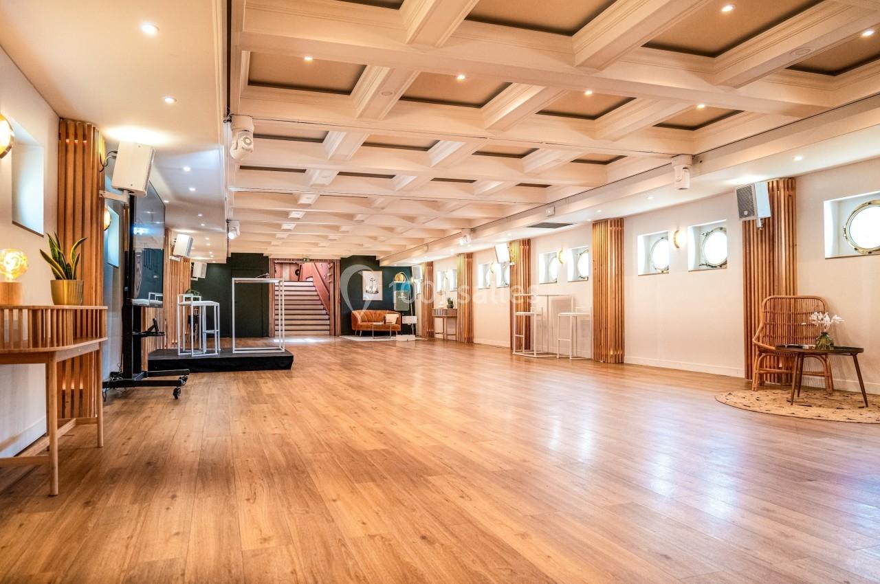 Salle lumineuse avec parquet en bois, plafond à caissons, mobilier minimaliste et escalier en arrière-plan.