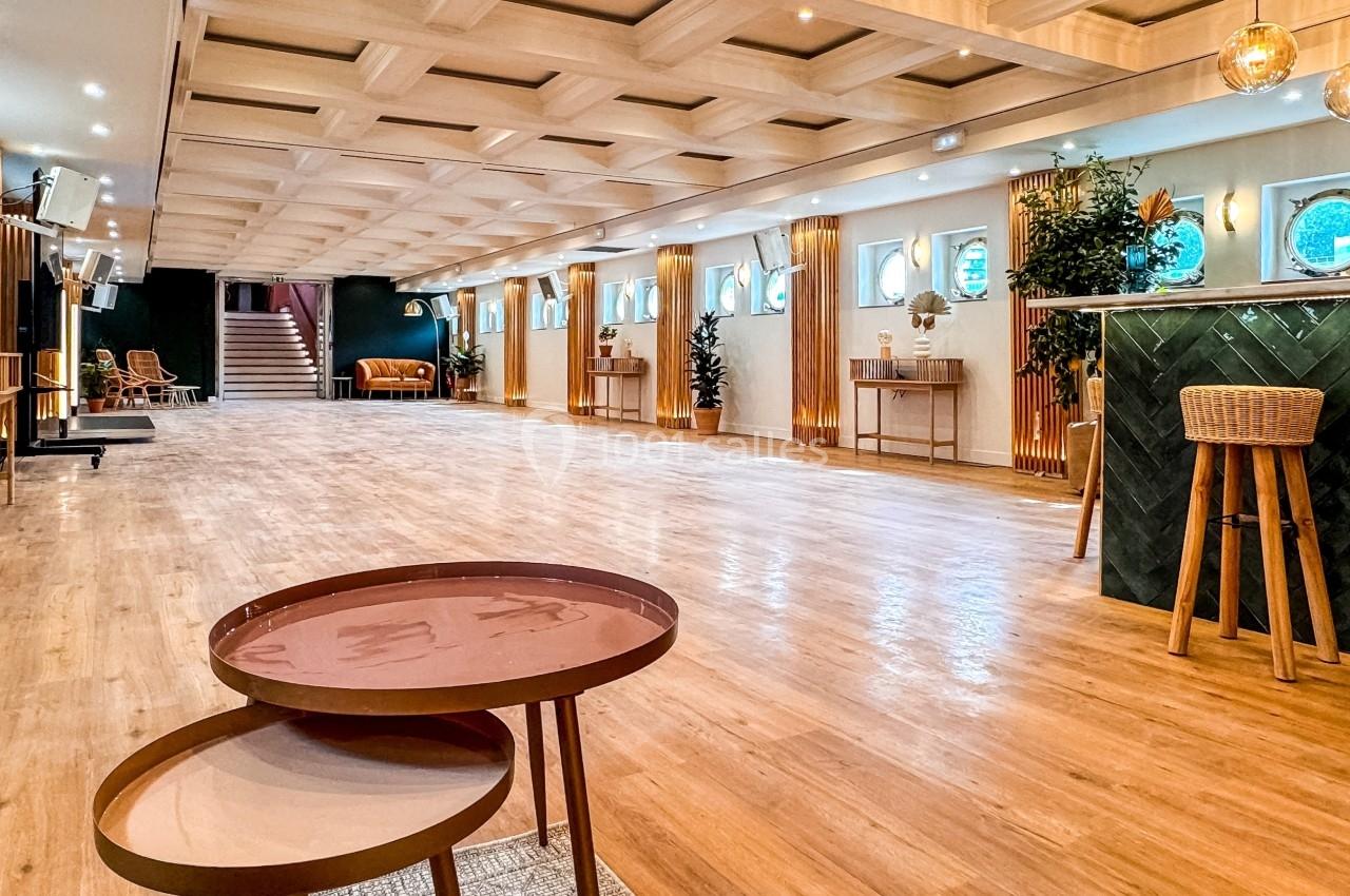 Salle spacieuse avec parquet clair, mobilier moderne, bar vert et éclairage chaleureux.