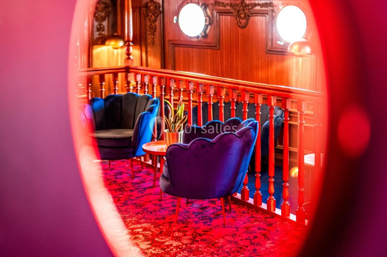 Vue d'un salon élégant avec fauteuils bleus, table basse et plante, encadré par une ouverture circulaire.