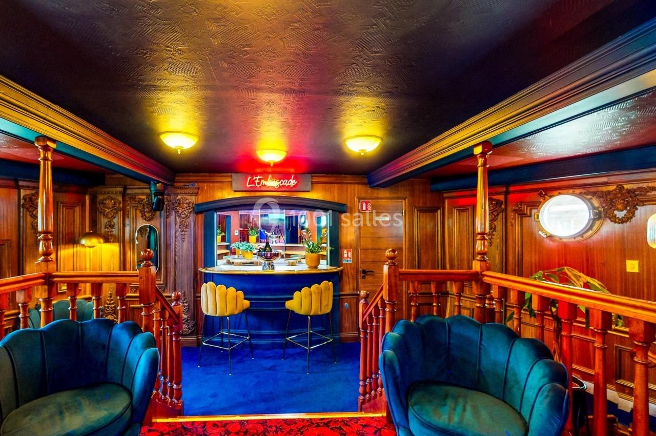 Intérieur d'un bar au style rétro avec fauteuils en velours, comptoir central et éclairage chaleureux.