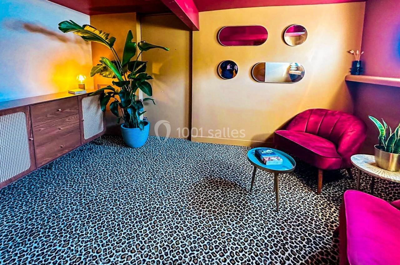 Salon coloré avec fauteuils rouges, tapis léopard, plantes en pot et murs jaunes ornés de miroirs ovales.