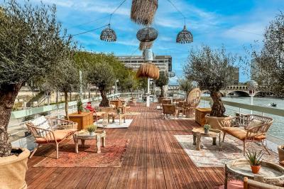 Entrée d'un restaurant aménagé sur un bateau, avec une passerelle en bois et des plantes en pot.