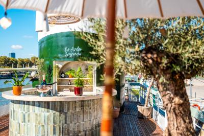 Entrée d'un restaurant aménagé sur un bateau, avec une passerelle en bois et des plantes en pot.