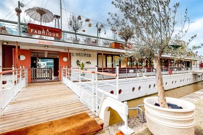 Entrée d'un restaurant aménagé sur un bateau, avec une passerelle en bois et des plantes en pot.