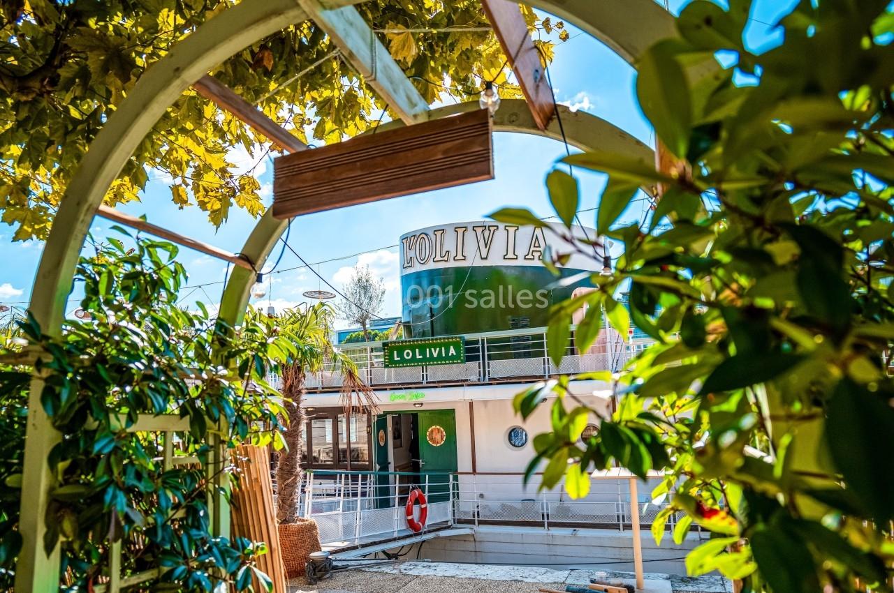 Vue d'un bateau nommé ’L'Olivia’ entouré de verdure, capturé à travers une arche végétalisée.