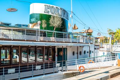 Entrée d'un restaurant aménagé sur un bateau, avec une passerelle en bois et des plantes en pot.