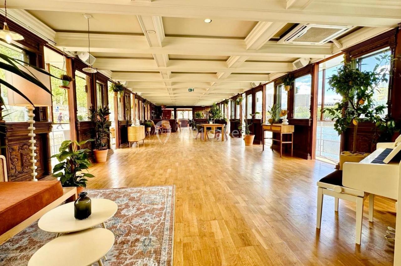 Salle lumineuse avec parquet, grandes fenêtres, plantes décoratives et mobilier en bois clair.