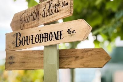 Panneau en bois indiquant les directions vers un jardin d'hiver et un boulodrome, entouré de verdure.