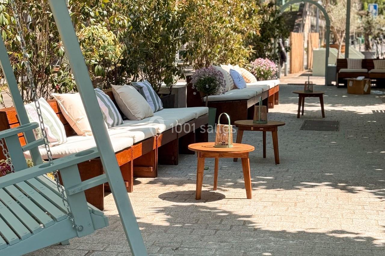 Bancs en bois avec coussins, table basse et verdure environnante sur une terrasse ensoleillée.