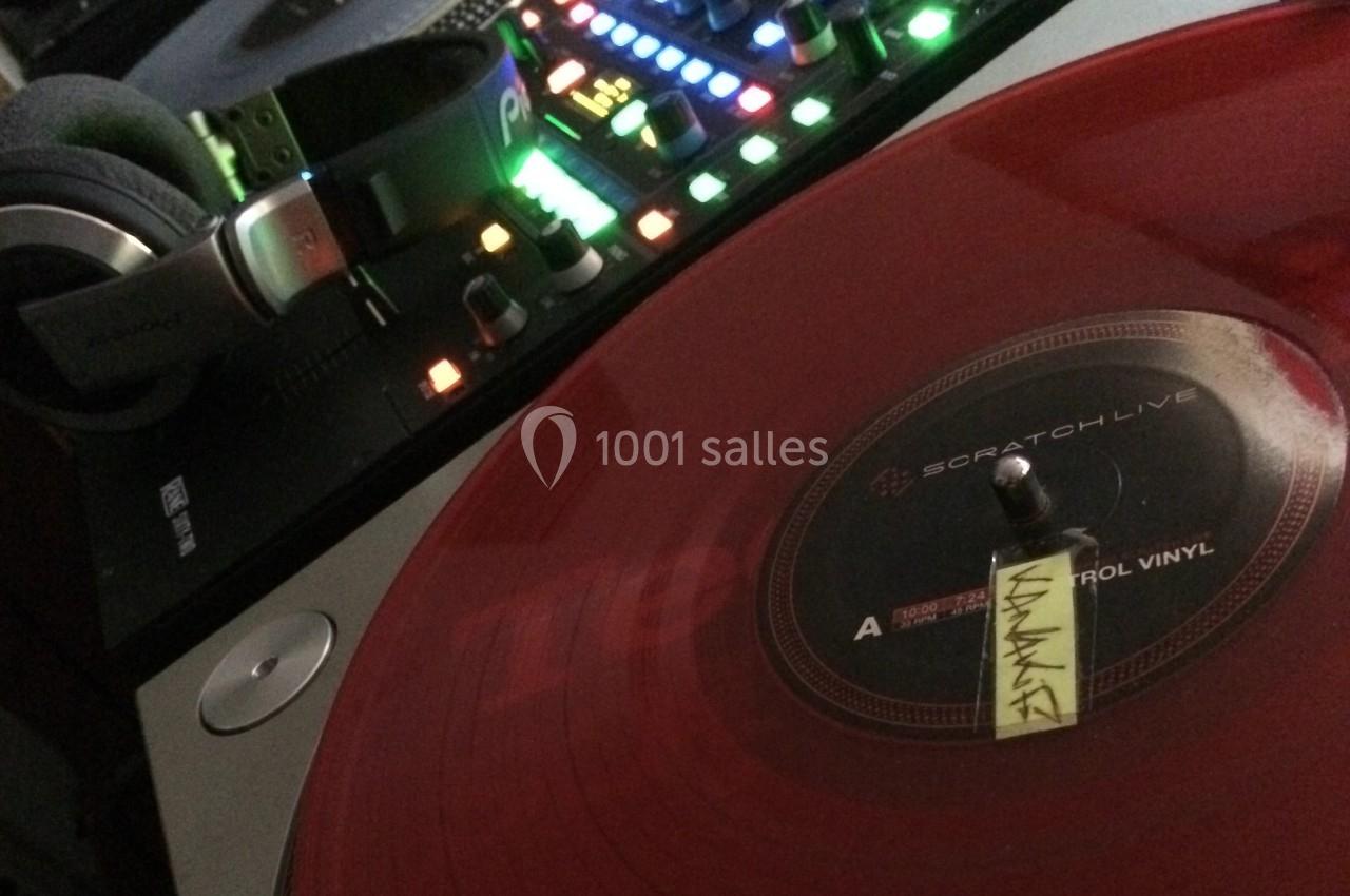 Platine vinyle rouge en lecture avec casque audio posé à côté et table de mixage lumineuse en arrière-plan.