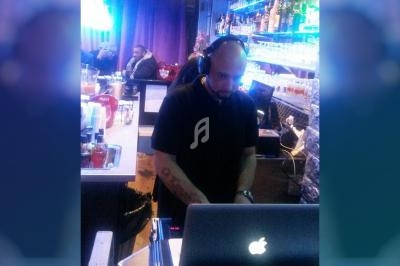 Un DJ portant un casque mixe de la musique sur un ordinateur portable dans un bar éclairé par des lumières bleues.