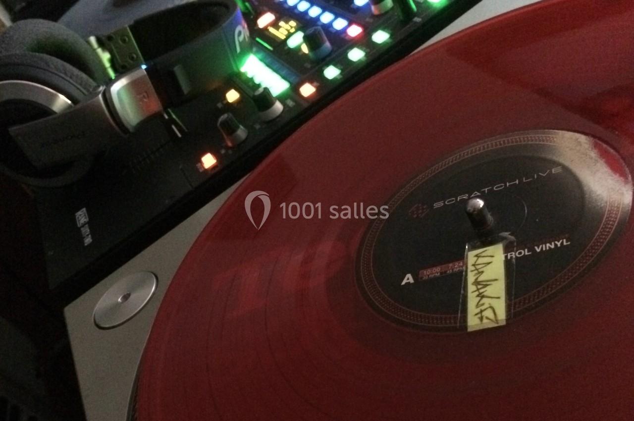 Platine vinyle avec disque rouge translucide en lecture, casque audio et table de mixage rétroéclairée en arrière-plan.