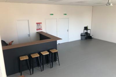 Salle lumineuse avec un comptoir en bois, quatre tabourets hauts, trois portes blanches et un coin avec ordinateur et…