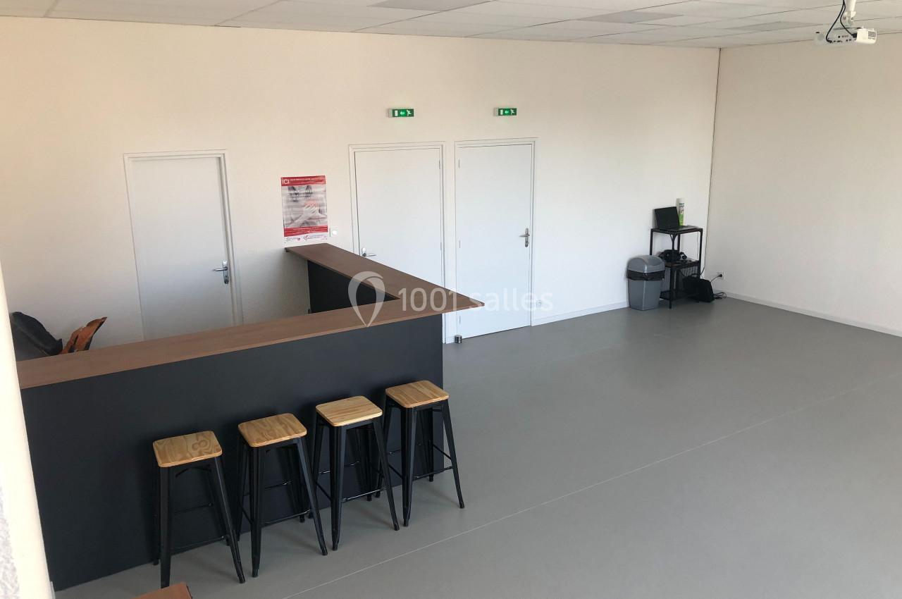 Salle lumineuse avec un comptoir en bois, quatre tabourets hauts, trois portes blanches et un coin avec ordinateur et…