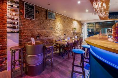 Intérieur d'un bar avec comptoir bleu éclairé, tabourets hauts, tables en bois et murs en briques apparentes.