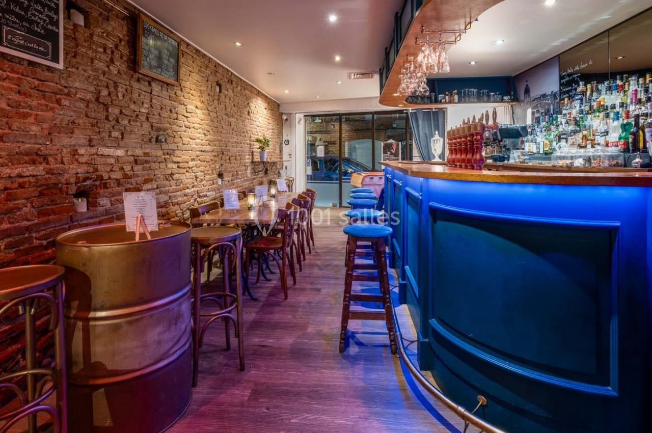 Bar à l'ambiance chaleureuse avec comptoir bleu éclairé, tabourets en bois et murs en briques apparentes.