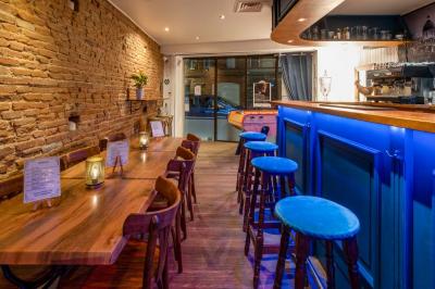 Intérieur d'un bar avec comptoir bleu éclairé, tabourets hauts, tables en bois et murs en briques apparentes.
