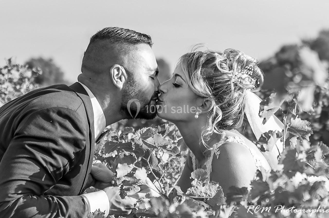 Un couple en tenue de mariage s'embrasse tendrement au milieu de vignes sous un ciel dégagé.