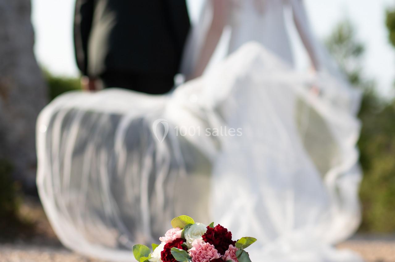 Un bouquet de fleurs posé au sol avec un couple de mariés flou en arrière-plan.