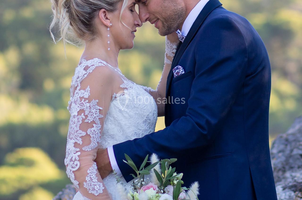 Un couple en tenue de mariage se tient tendrement face à face dans un cadre naturel verdoyant.