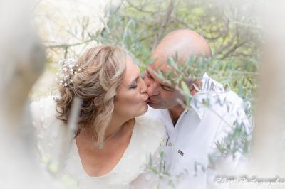 Un couple s'embrasse tendrement dans un cadre naturel entouré de branches d'olivier.