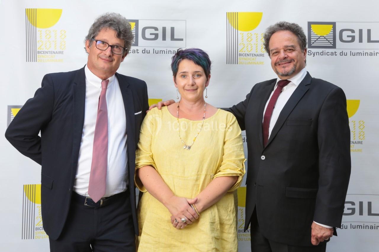 Trois personnes posent devant un fond avec le logo du Syndicat du Luminaire lors d'un événement officiel.