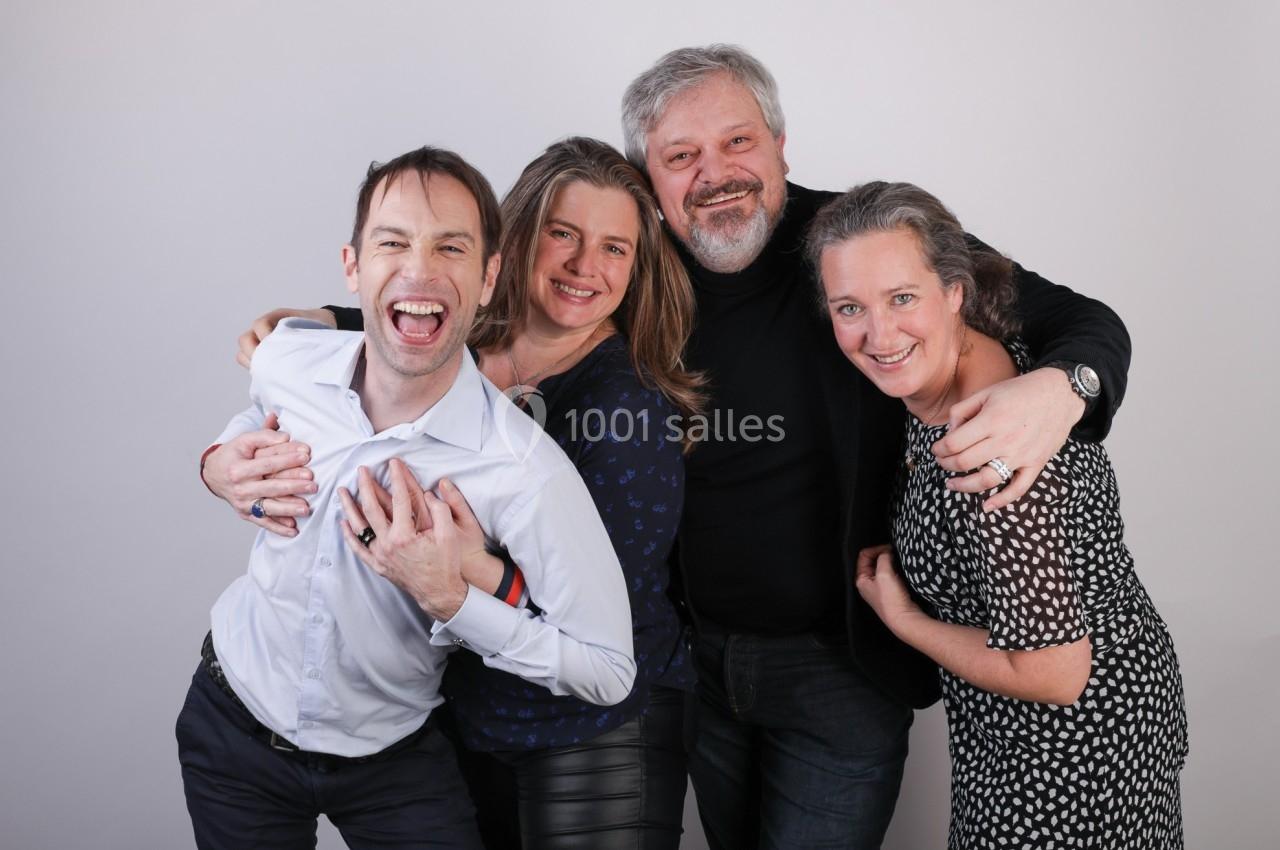 Quatre personnes souriantes posent ensemble devant un fond uni, exprimant joie et complicité.