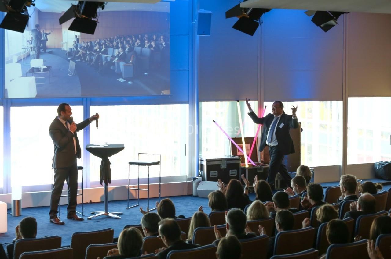 Un conférencier s'adresse à un public assis dans une salle, avec une projection d'image en arrière-plan.