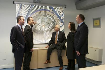 Femme portant des lunettes et un blazer à carreaux, posant devant un fond clair.