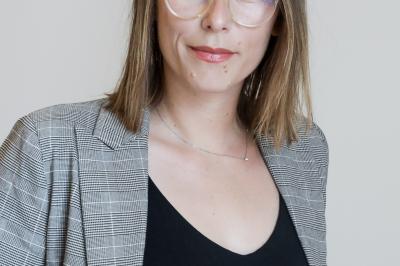 Femme portant des lunettes et un blazer à carreaux, posant devant un fond clair.