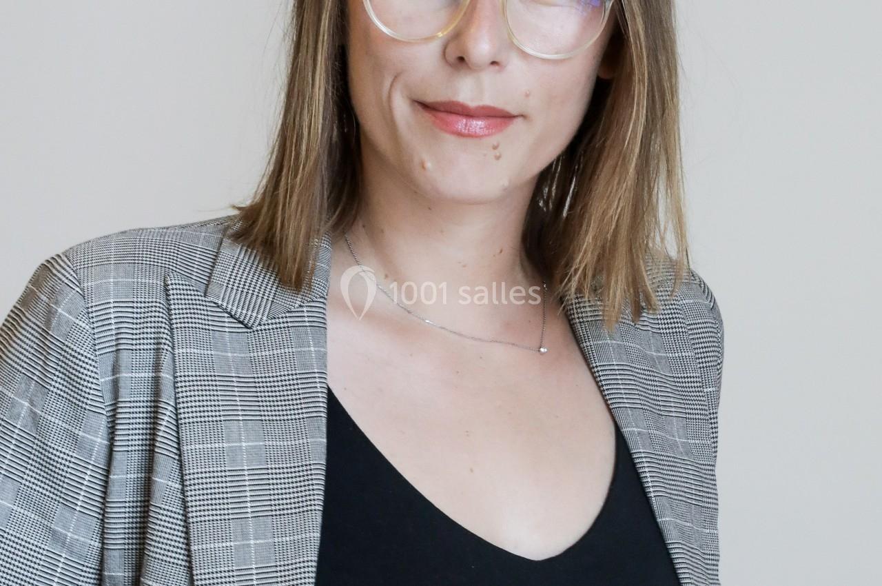 Femme portant des lunettes et un blazer à carreaux, posant devant un fond clair.