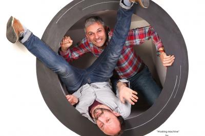 Femme souriante portant un blazer imprimé coloré, un t-shirt gris et un jean, posant devant un fond blanc.