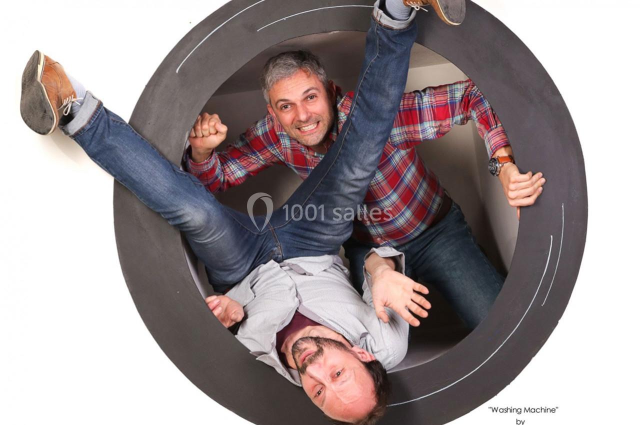 Deux hommes posent de manière humoristique à l'intérieur d'une structure circulaire ressemblant à un tambour de machine à…