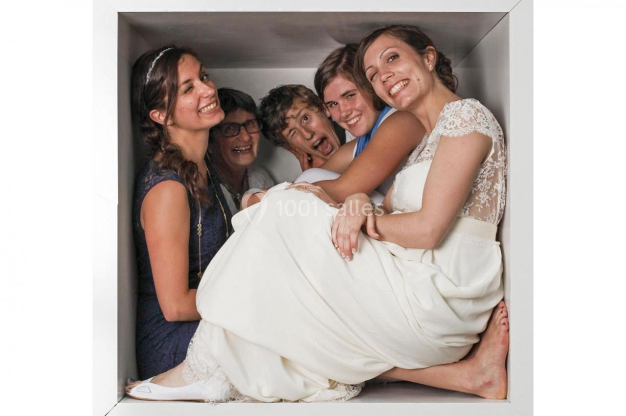 Cinq personnes souriantes, dont une en robe de mariée, assises ensemble dans un espace confiné blanc.