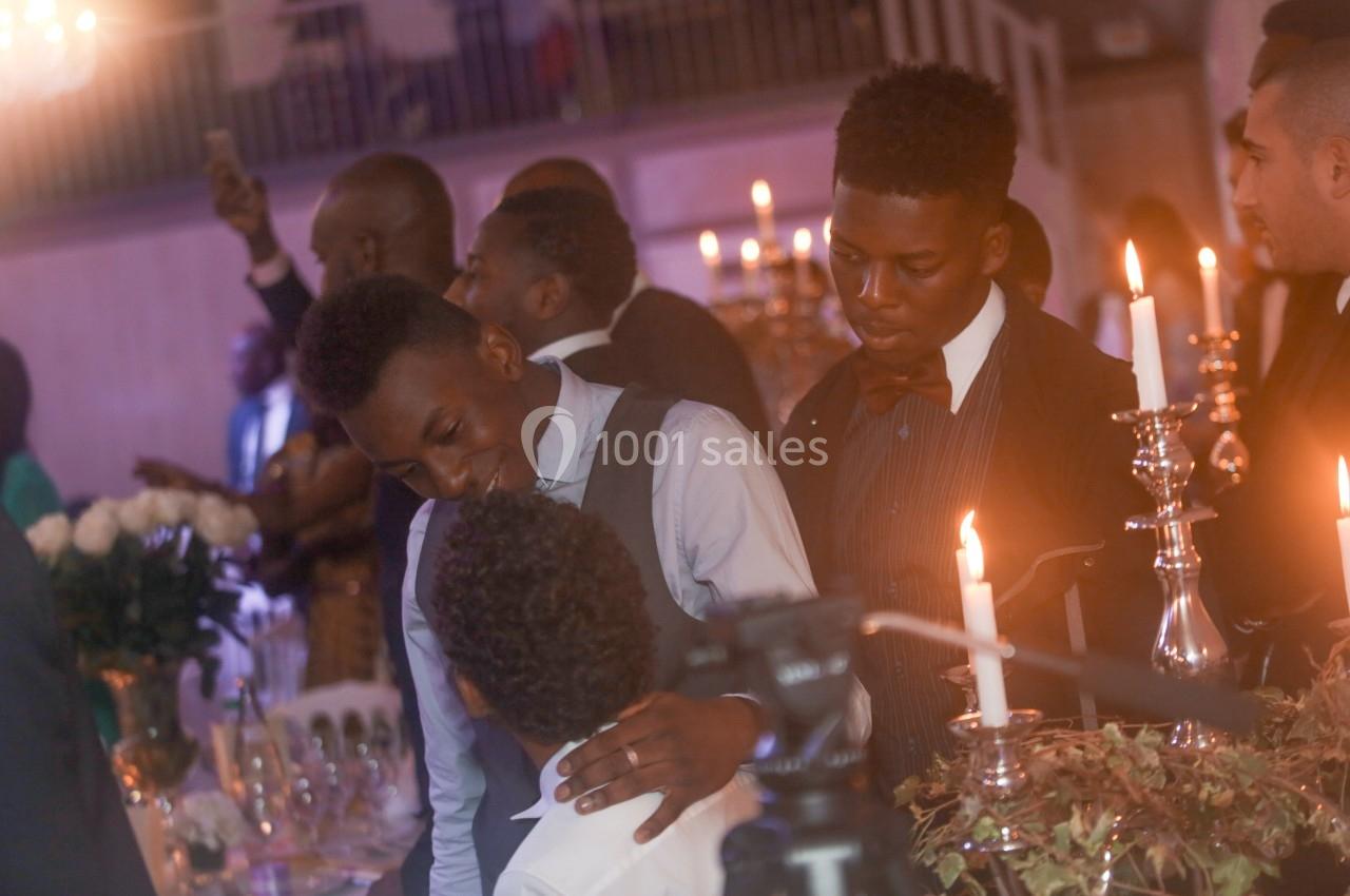 Des personnes élégamment vêtues discutent autour d'une table décorée de chandeliers dans une ambiance festive.