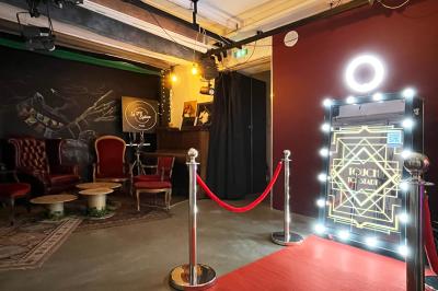 Femme souriante portant un blazer imprimé coloré, un t-shirt gris et un jean, posant devant un fond blanc.