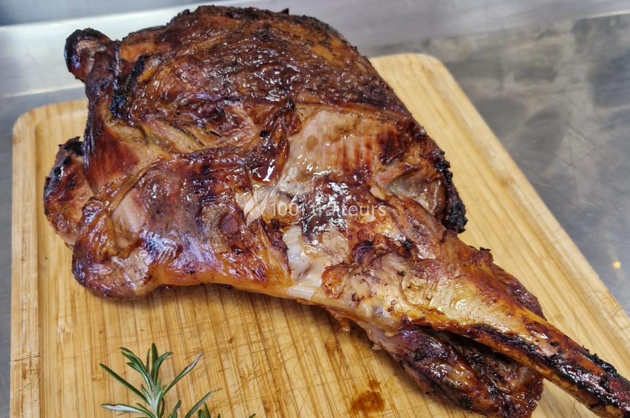 Gigot d'agneau rôti posé sur une planche en bois, accompagné d'une branche de romarin.