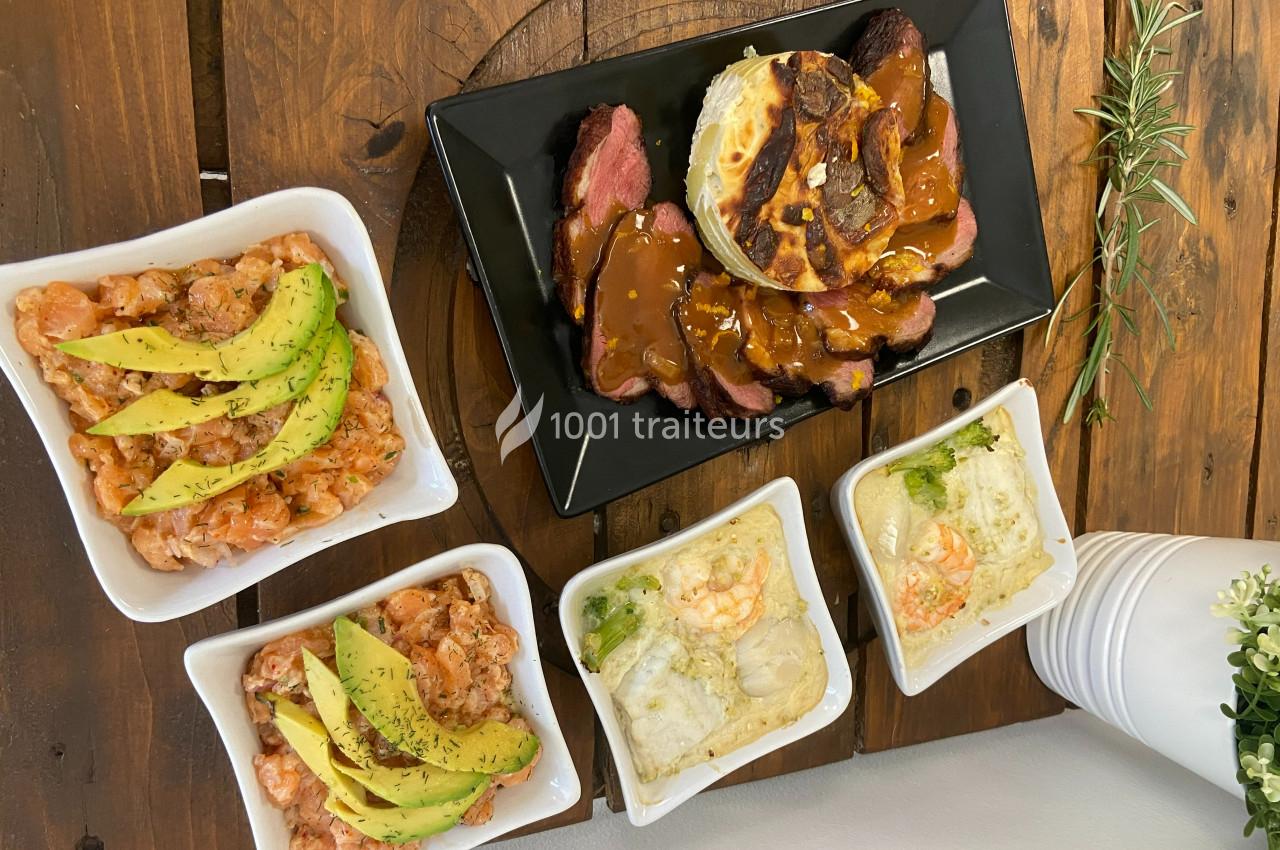 Assortiment de plats comprenant des crevettes à l'avocat, gratins et viande avec sauce, disposés sur une table en bois.