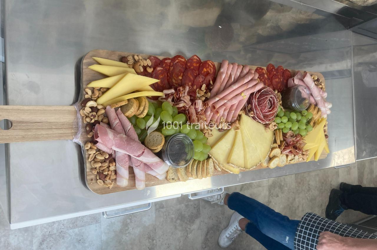 Plateau en bois garni de charcuteries, fromages, fruits secs, raisins, pains et condiments, présenté sur une table.