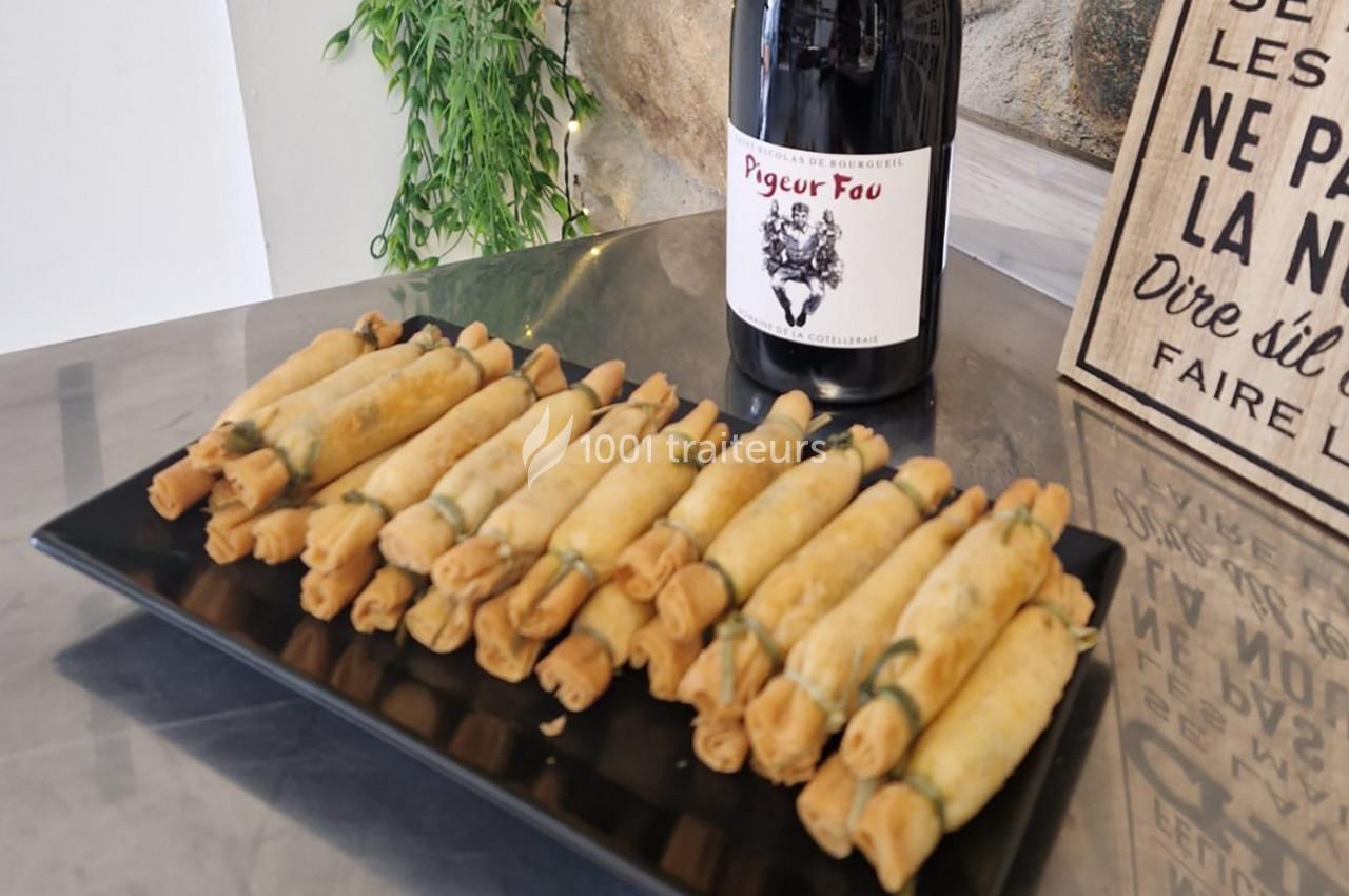 Assiette de rouleaux frits alignés sur une table, accompagnée d'une bouteille de vin rouge.