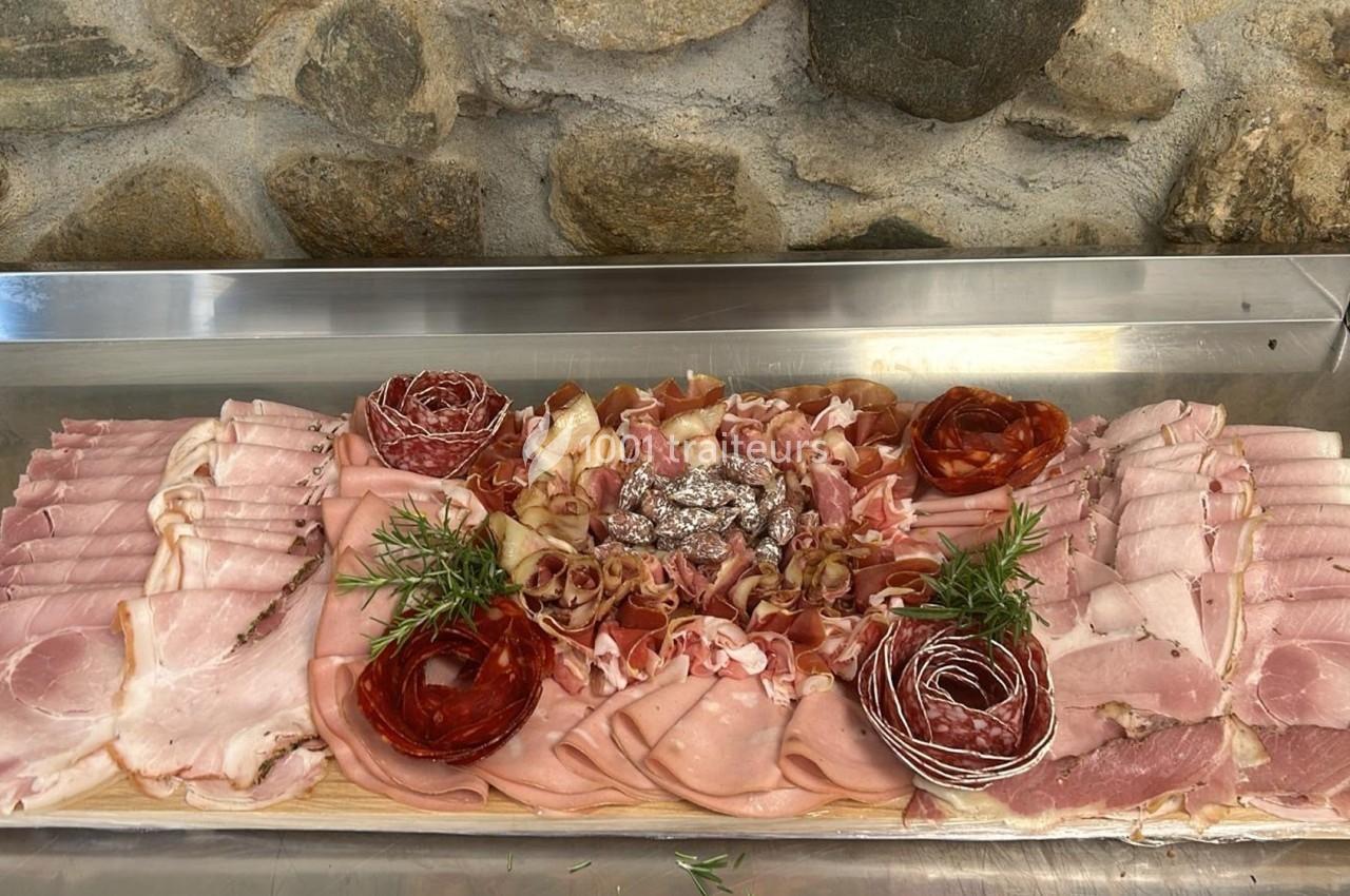 Plateau de charcuterie variée avec jambon, saucisson, rosettes et herbes fraîches, présenté sur une planche en bois.