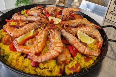Plat de paella avec crevettes, riz jaune, poivrons rouges, rondelles de chorizo et quartiers de citron.