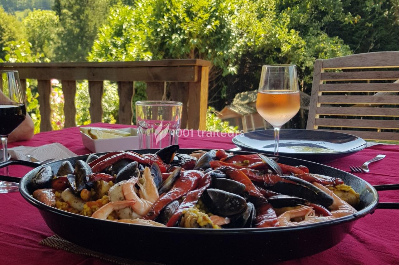 Plat de paella aux fruits de mer servi sur une table en extérieur, accompagné de verres de vin et d'eau.