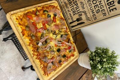 Pizza garnie de jambon cru, olives noires, artichauts, tomates séchées, fromage râpé et filet de pesto.