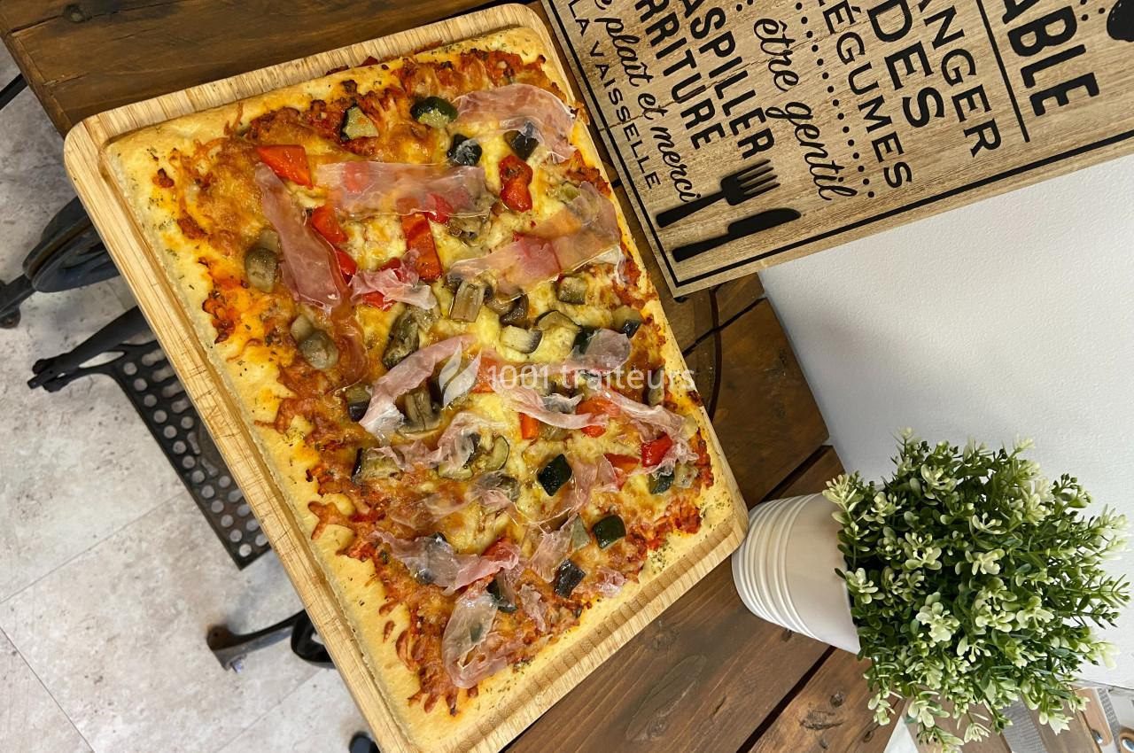 Pizza rectangulaire garnie de jambon cru, champignons, poivrons et olives, servie sur une planche en bois.