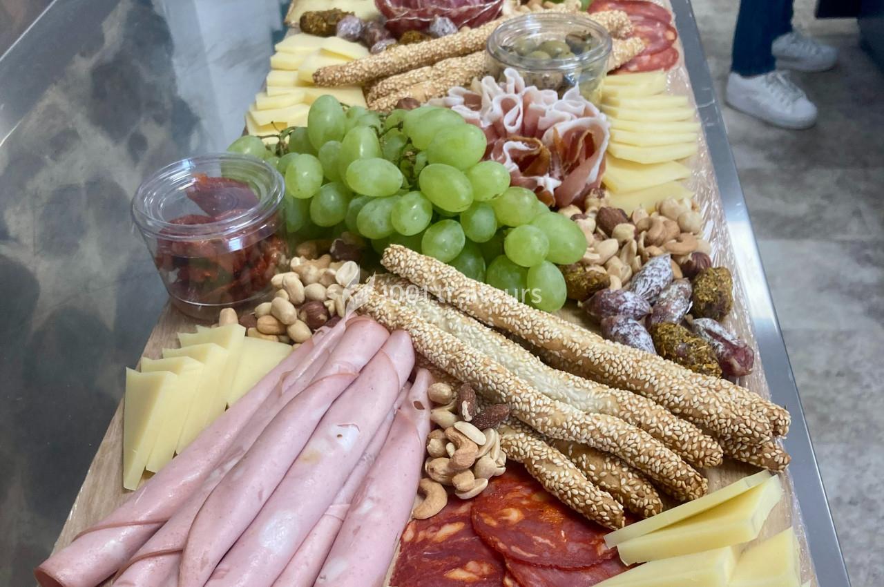 Plateau garni de charcuterie, fromages, raisins, fruits secs, gressins et condiments, présenté sur une table.
